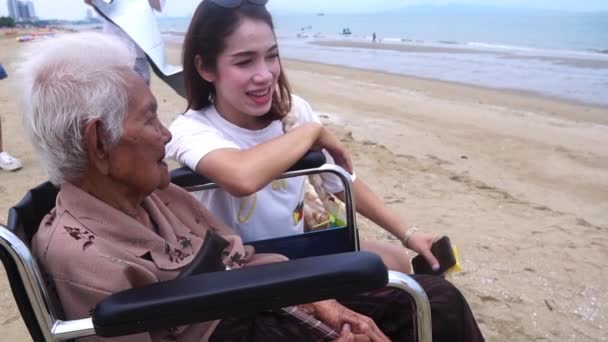 镜头慢动作 老妇人坐在沙滩上的轮椅上 微笑着和女儿说话 — 图库视频影像