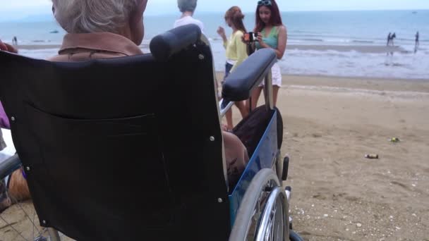 古い母親が車椅子に座って 砂浜の子供たちを幸せに見ています — ストック動画