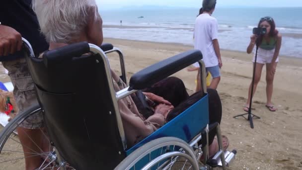一位年老的母亲坐在轮椅上 在沙滩上高兴地看着孩子们 — 图库视频影像