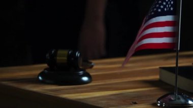 Amerikan bayrağı sallıyor, tokmak ve kitap ahşap masada, arka planda kadın yargıç