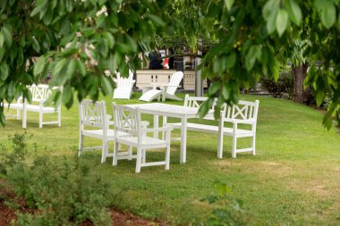 Ağaçların altındaki bahçede beyaz sandalyeler ve masa