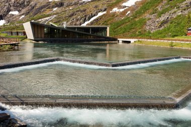 Trollstigen Kafe 'nin modern üçgen binası ve dağların önündeki ziyaretçi merkezi. Norveç