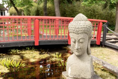 Japon bahçesindeki kırmızı köprünün önündeki heykel