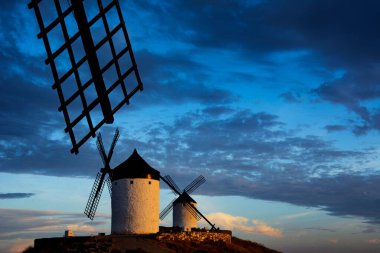 Windmills at sunset in Consuegra, population of Toledo, Spain. In the foreground is a blade belonging to another windmill.