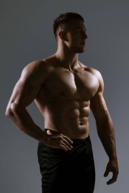 Formda bir erkek model, etkileyici bir pozda gücünü gösterir. Etkileyici bir ışık altında, fiziğini ön plana çıkarır.