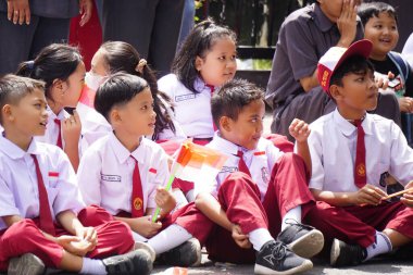 Endonezyalı ilkokul öğrencileri ve arkadaşları ellerinde kırmızı ve beyaz bayraklar tutuyorlar.