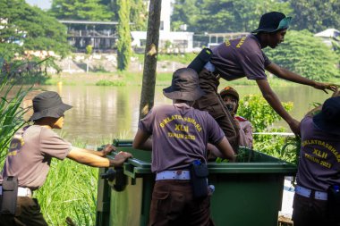 İnsanlar çöpleri temizleyerek ve yabani otları temizleyerek çevreyi temizliyorlar..
