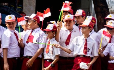 Indonesian elementary school students with uniform bring indonesian flag happily on the street