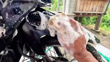 El çamaşır yıkarken bir motosikleti köpükle temizliyor.