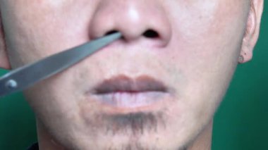 Sakallı Endonezyalı adam burun kıllarını makas kullanarak tıraş ediyor.