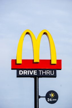 Bir McD (McDonalds) logosu, McD restoranındaki gökyüzü arkaplanlı sürücü kutusuyla birlikte ışık kutusu direğinde görüntülenir.