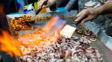 Satıcı kuyrukta bekleyen müşteriler için ızgara kalamar pişirir..