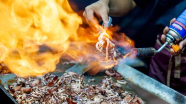 Satıcı kuyrukta bekleyen müşteriler için ızgara kalamar pişirir..