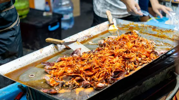 Satıcı kuyrukta bekleyen müşteriler için ızgara kalamar pişirir..