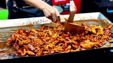 Satıcı kuyrukta bekleyen müşteriler için ızgara kalamar pişirir..