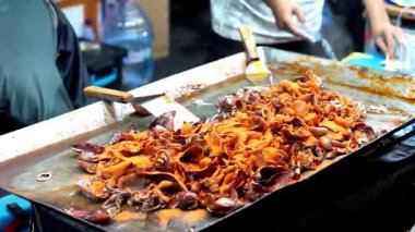 Satıcı kuyrukta bekleyen müşteriler için ızgara kalamar pişirir..