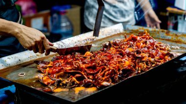 Satıcı kuyrukta bekleyen müşteriler için ızgara kalamar pişirir..