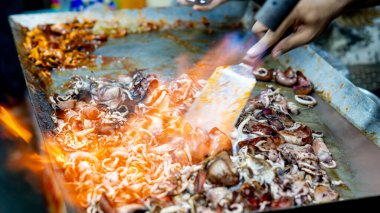 Satıcı kuyrukta bekleyen müşteriler için ızgara kalamar pişirir..