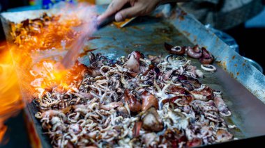 Satıcı kuyrukta bekleyen müşteriler için ızgara kalamar pişirir..