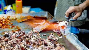 Satıcı kuyrukta bekleyen müşteriler için ızgara kalamar pişirir..