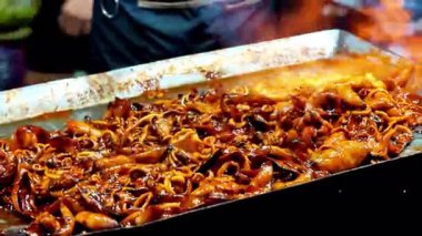 Satıcı kuyrukta bekleyen müşteriler için ızgara kalamar pişirir..