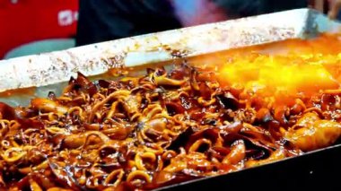 Satıcı kuyrukta bekleyen müşteriler için ızgara kalamar pişirir..