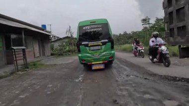 Asfalt yol araçların geçtiği deliklerle dolu, bazıları kuru, bazıları su altında.
