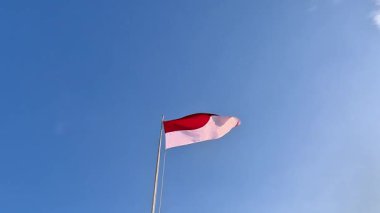 Mavi arka planda dalgalanan bir direkte kırmızı ve beyaz bayrak.