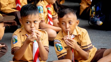 Endonezyalı izci öğrenci parkta mutlu bir şekilde bambu flütü çalıyor.