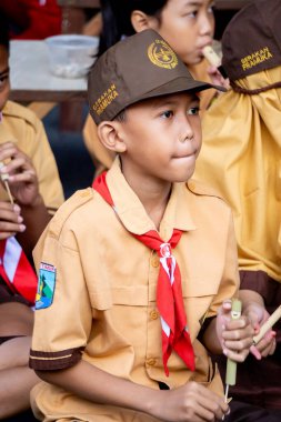Endonezyalı izci öğrenci parkta mutlu bir şekilde bambu flütü çalıyor.