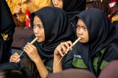 Endonezyalı izci öğrenci parkta mutlu bir şekilde bambu flütü çalıyor.