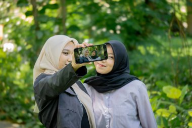 Two beautiful sibling Asian women taking a selfie together in the park.
