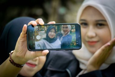 Two beautiful sibling Asian women taking a selfie together in the park.