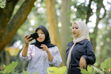 Two beautiful sibling Asian women taking a selfie together in the park.