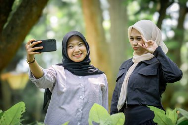 Two beautiful sibling Asian women taking a selfie together in the park.