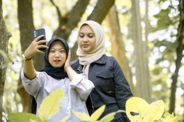 Two beautiful sibling Asian women taking a selfie together in the park.