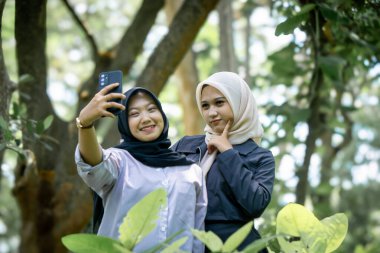 Two beautiful sibling Asian women taking a selfie together in the park.