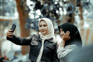 Two beautiful sibling Asian women taking a selfie together in the park.