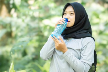 Muslim woman drinking bottled isotonic drink after exercising in the park
