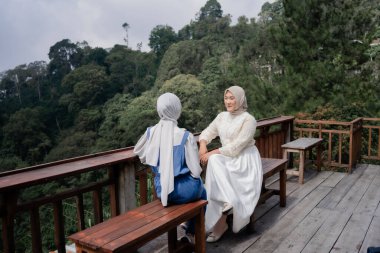Two beautiful asian moslem women talking together at quiet cafe with blue sky background