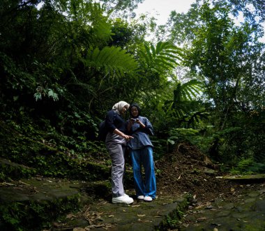 Two beautiful asian moslem girl take a picture at the green forest