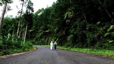 Two Muslim Asian women walking on a quiet highway with trees around the road. Bathing forest.