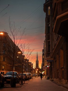 Gün batımında Riga 'da Gertrude Caddesi' nde, batan güneşin sıcacık parıltısı manzarayı aydınlatıyor. Arka planda, Gertrude Kilisesi, sakin kentsel manzaraya tarihi bir dokunuş ekleyerek dimdik ayakta duruyor..