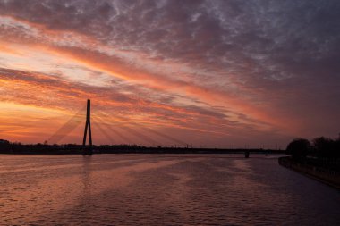 Riga 'daki Vansu Köprüsü üzerinde Akmens Köprüsü' nden çekilen güzel bir günbatımı. Gökyüzü turuncu ve mor tonlarda boyanır, ikonik köprü için çarpıcı bir zemin oluşturur..