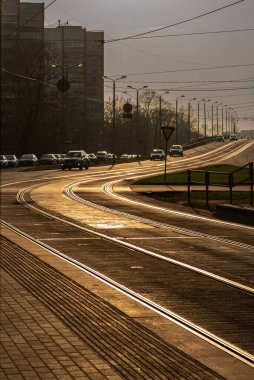Riga, Letonya 'da bir sokak. Günışığı kıvrımlı tramvay rayları, Sovyet döneminden kalma apartmanlar ve arka planda arabalarla birlikte olay yerinden geçiyor. Sıcak, nostaljik atmosfer.