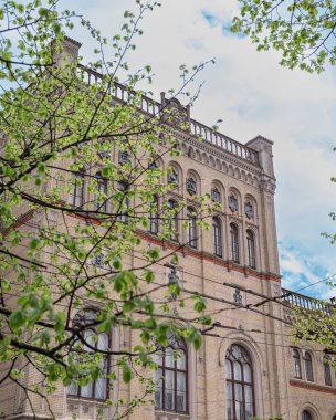 Letonya Üniversitesi 'nin baharda açtığı ağaçlar ve parlak güneş ışığıyla çerçevelenen perdesi. Riga 'nın kalbindeki akademik miras ve mevsimsel güzelliğin uyumlu bir karışımı..