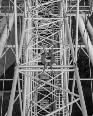 Riga, Letonya 'daki dönme dolabın yapısal detaylarını gösteren siyah beyaz bir fotoğraf. Görüntü, gökyüzüne karşı metal iskeletin karmaşık geometrisini ve kontrastını vurgular. 