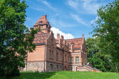 Yaz boyunca açık bir gökyüzü altında yemyeşil ile çevrili Letonya 'daki Jaunmokas Sarayı manzarası.