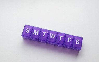 İlaç, vitamin depolama ve günlük dozaj planlaması için kullanılan, beyaz bir zemin üzerinde izole edilmiş, her gün için ayrı bölümleri olan mor haftalık hap organizatörü..