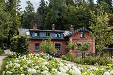 Yeşil ağaçlar ve çiçek açan beyaz ortancalarla çevrili güzel, eski kırmızı tuğla bir binanın manzarası. Tarihi mimari bereketli doğayla uyum içinde, romantik ve resimsel bir atmosfer yaratıyor..
